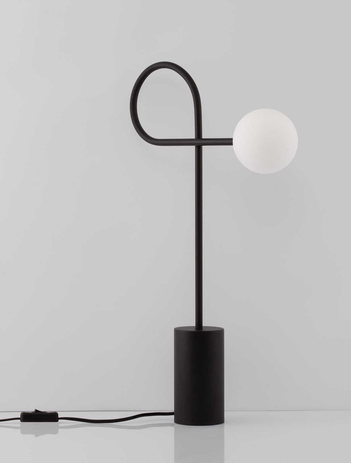 Silhouette de la lampe éteinte, socle cylindrique et tige fine formant boucle