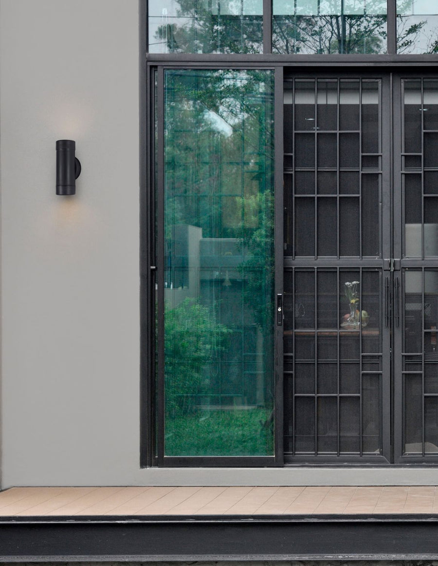 Luminaire noir installé sur mur gris près d'une grande porte vitrée
