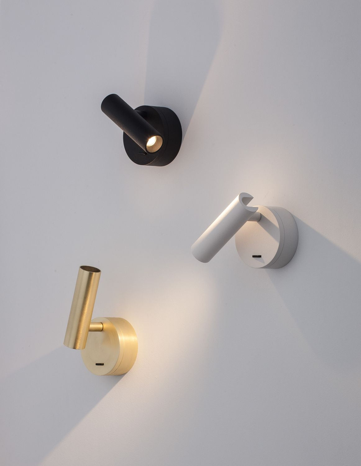 Trois appliques murales en finitions noire, blanche et laiton sur un mur