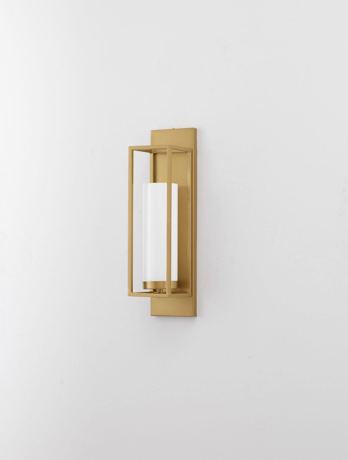 Applique murale dorée montée sur un mur blanc, verre opalin cylindrique.