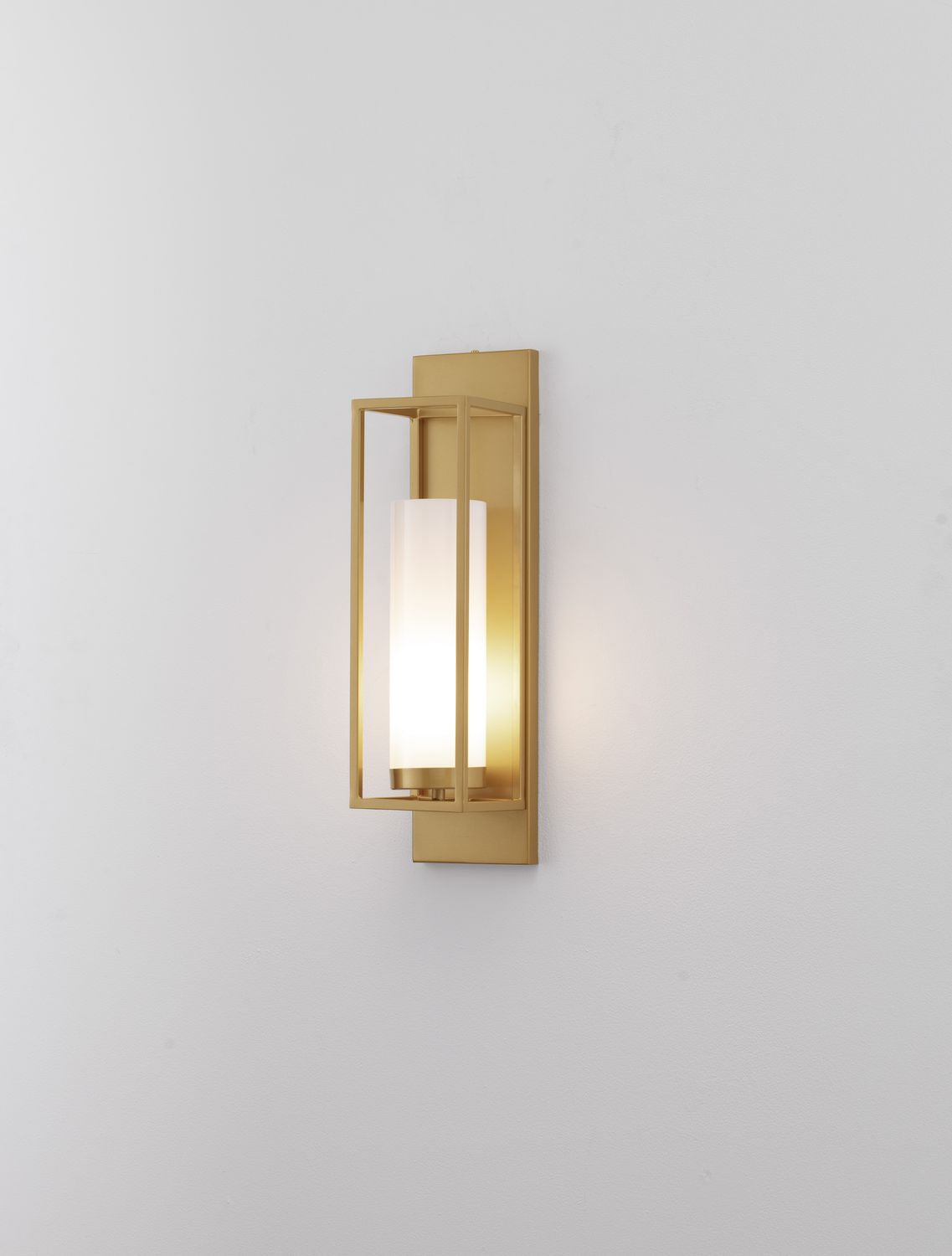 Applique murale dorée allumée sur mur blanc, lumière chaude diffusée.