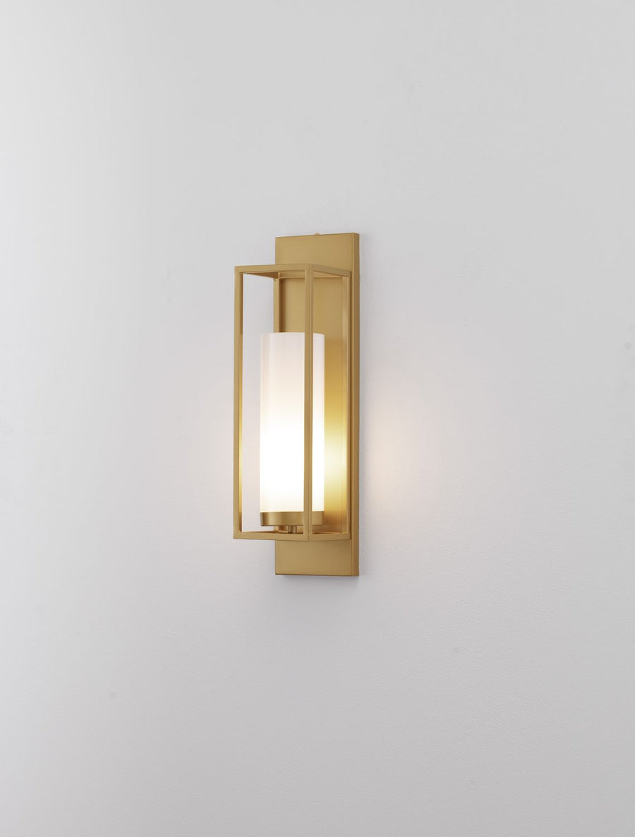 Applique murale dorée allumée sur mur blanc, lumière chaude diffusée.
