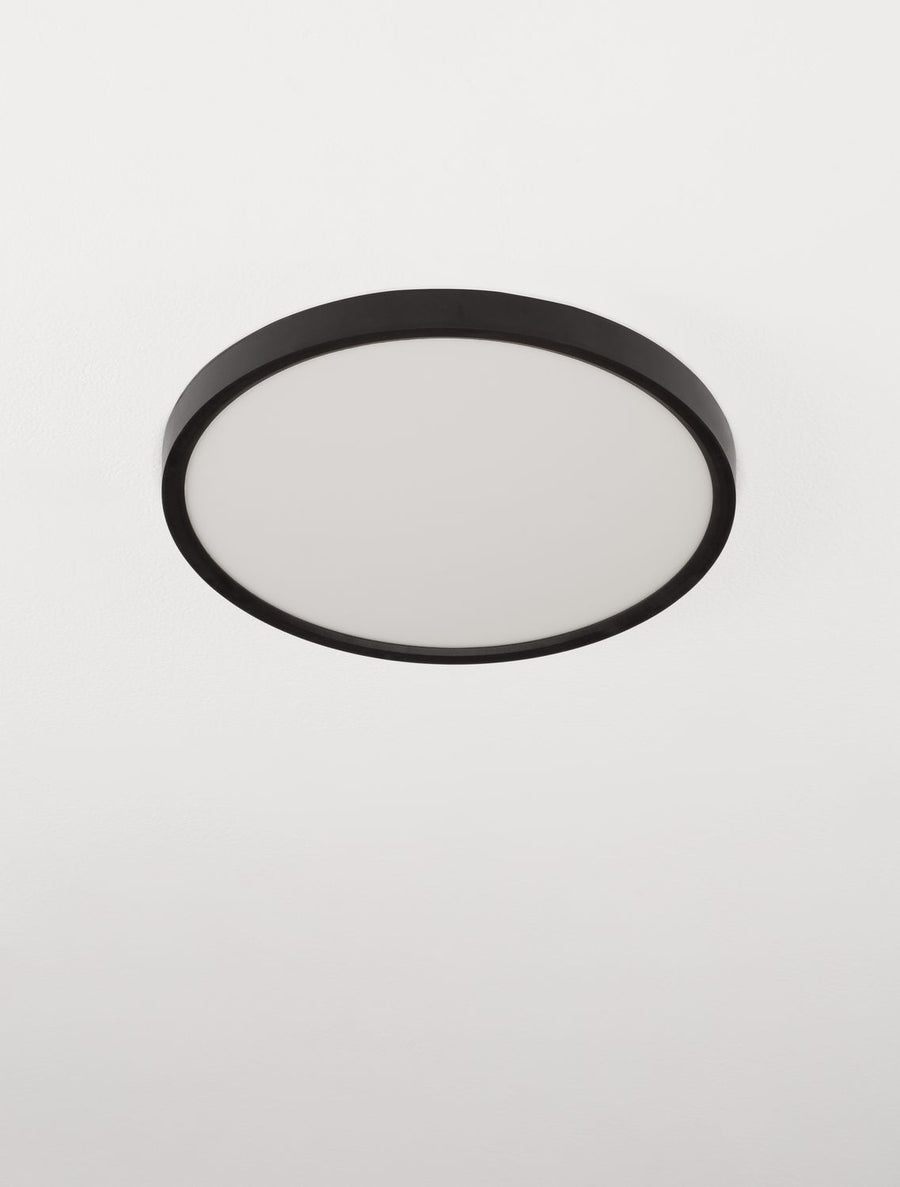 Plafonnier circulaire noir vu de biais, large diffuseur blanc opale au centre.