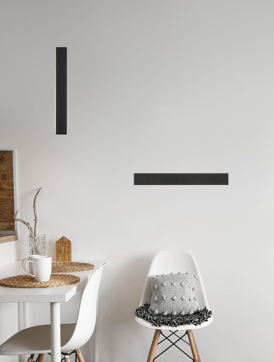 Applique murale noire verticale fixée sur un mur blanc dans un intérieur lumineux