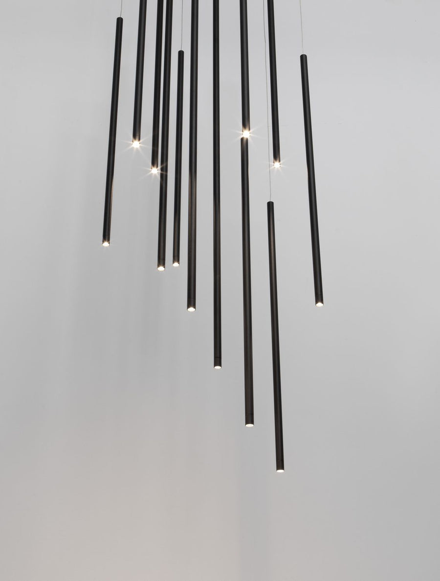 Gros plan sur des tiges noires suspendues, sources lumineuses allumées sur fond gris clair