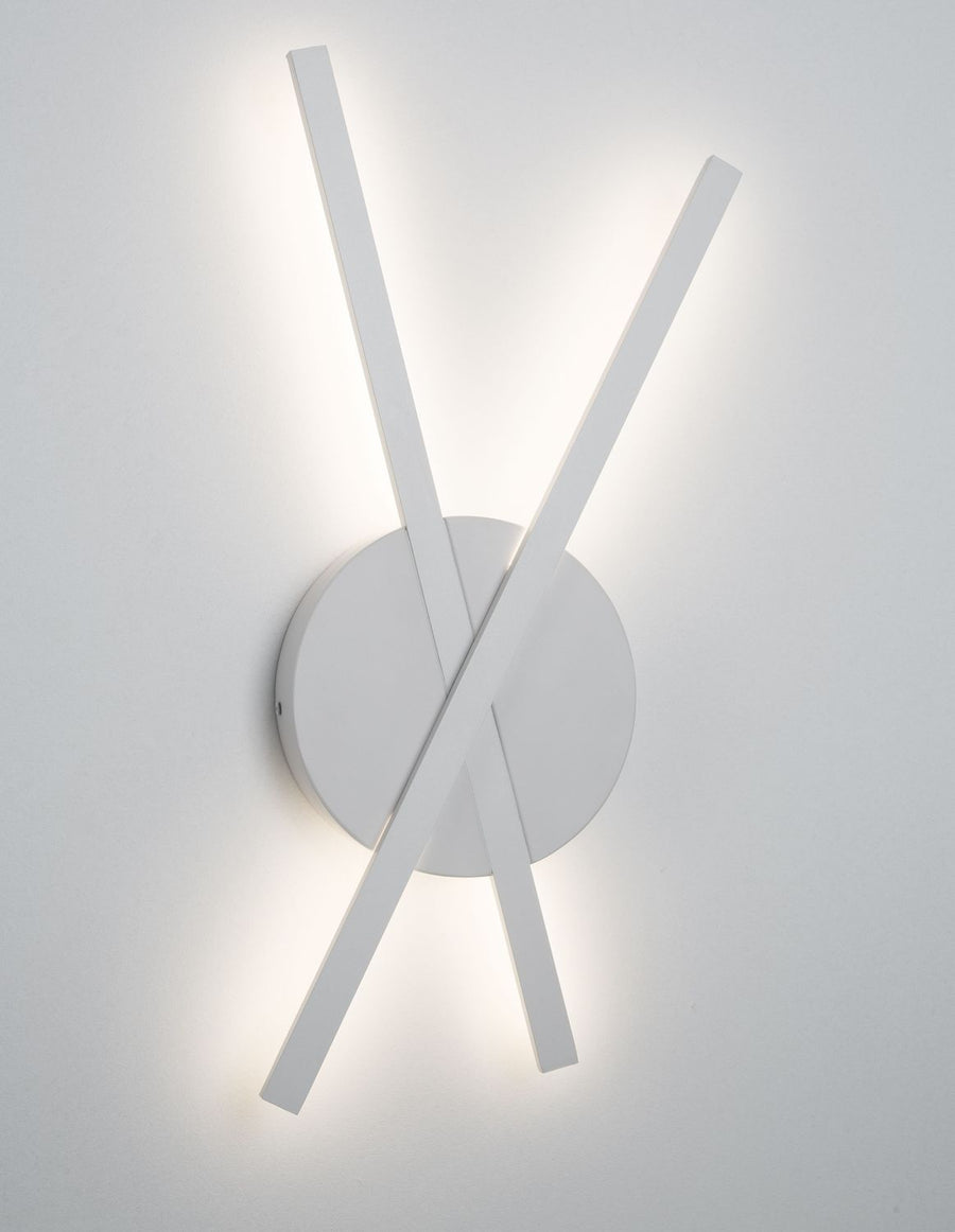 Applique murale blanche allumée, deux barres croisées sur base ronde, halo lumineux.