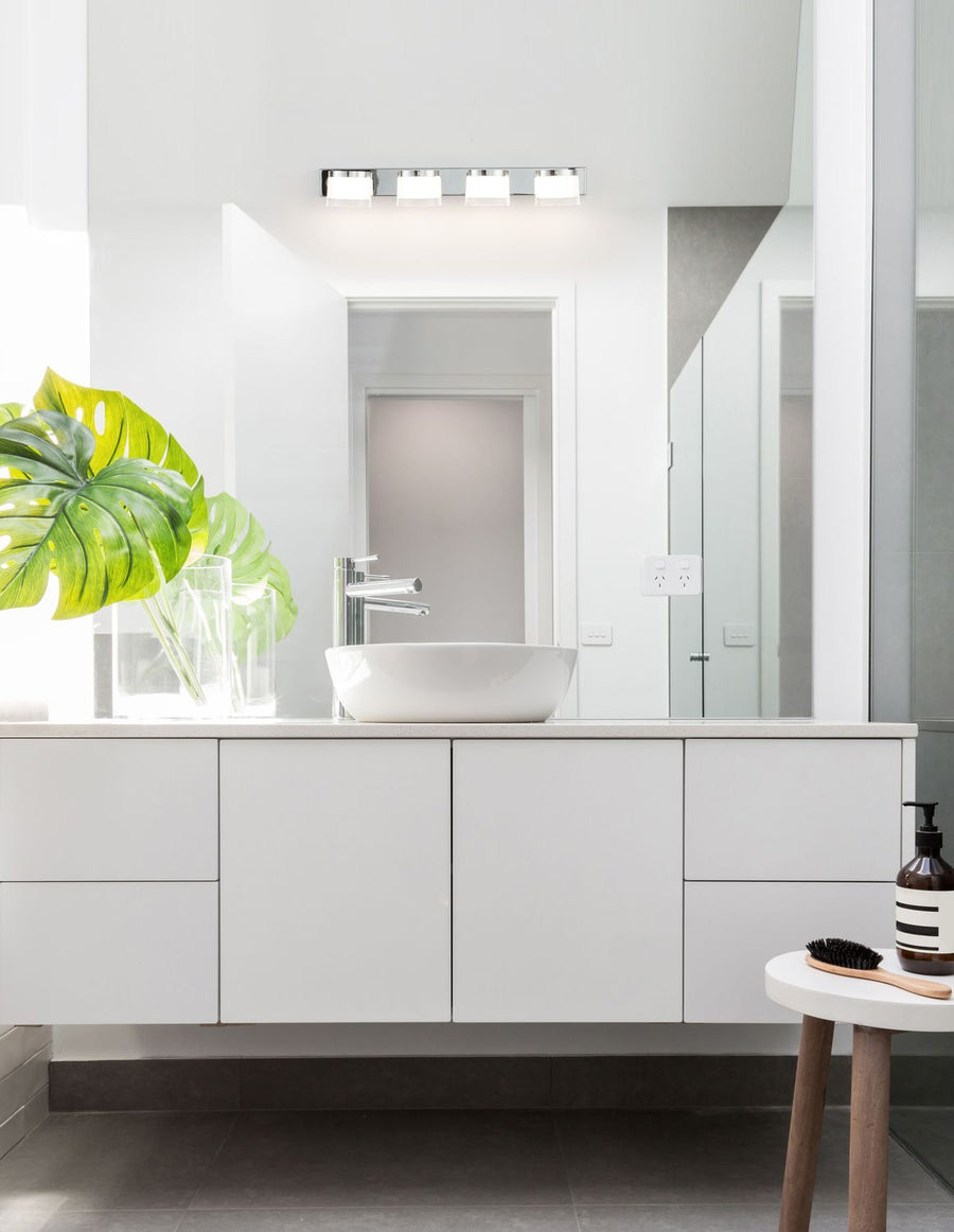 Applique chromée à quatre lumières installée au-dessus d'un miroir de salle de bain blanche