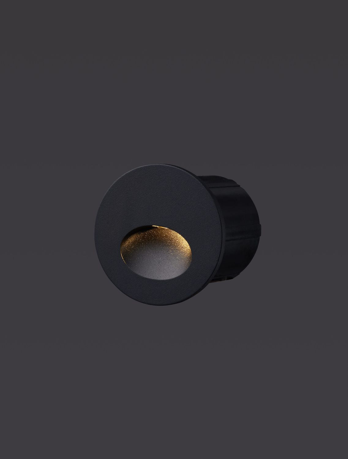 Luminaire encastré noir allumé, diffusant une lumière chaude dans son ouverture.
