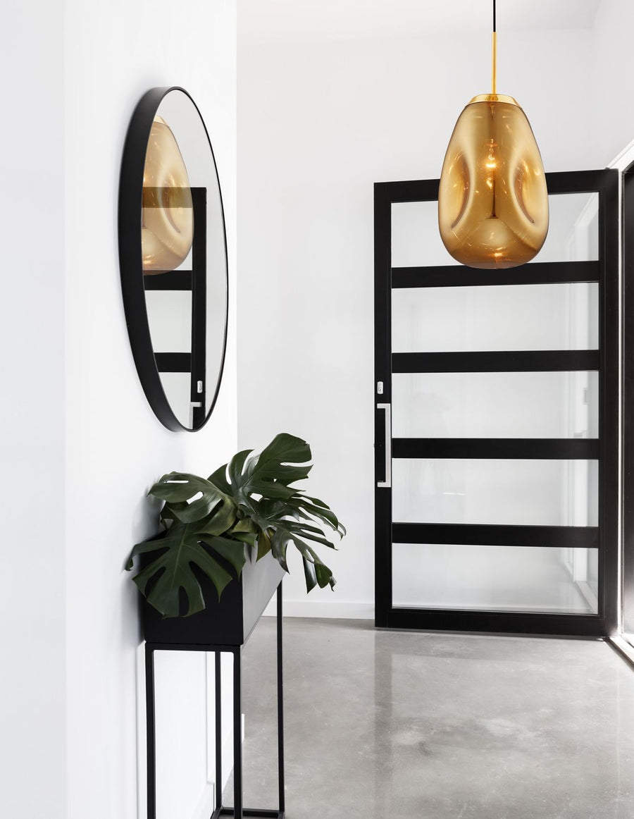 Suspension dorée en verre ambré éclairant une entrée blanche avec miroir rond noir