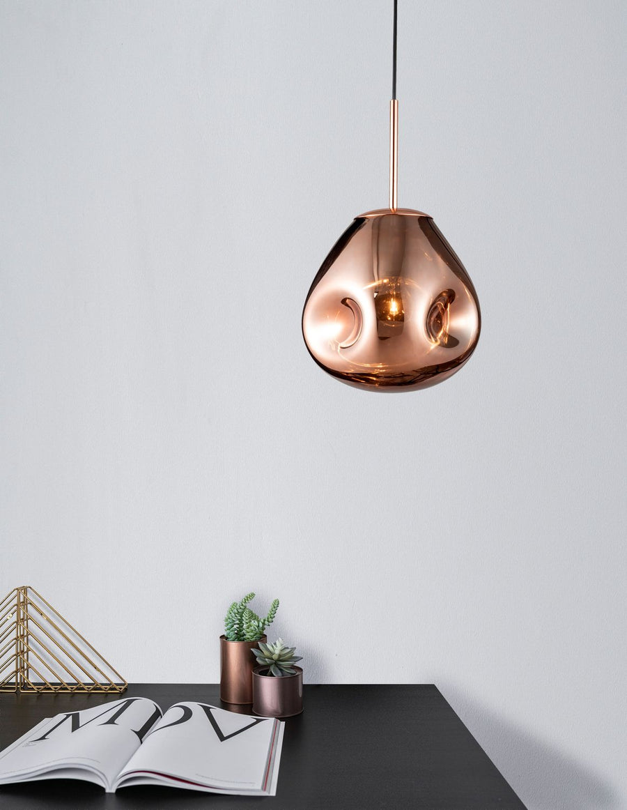 Suspension cuivrée installée au-dessus d'un bureau noir avec livres et plantes.
