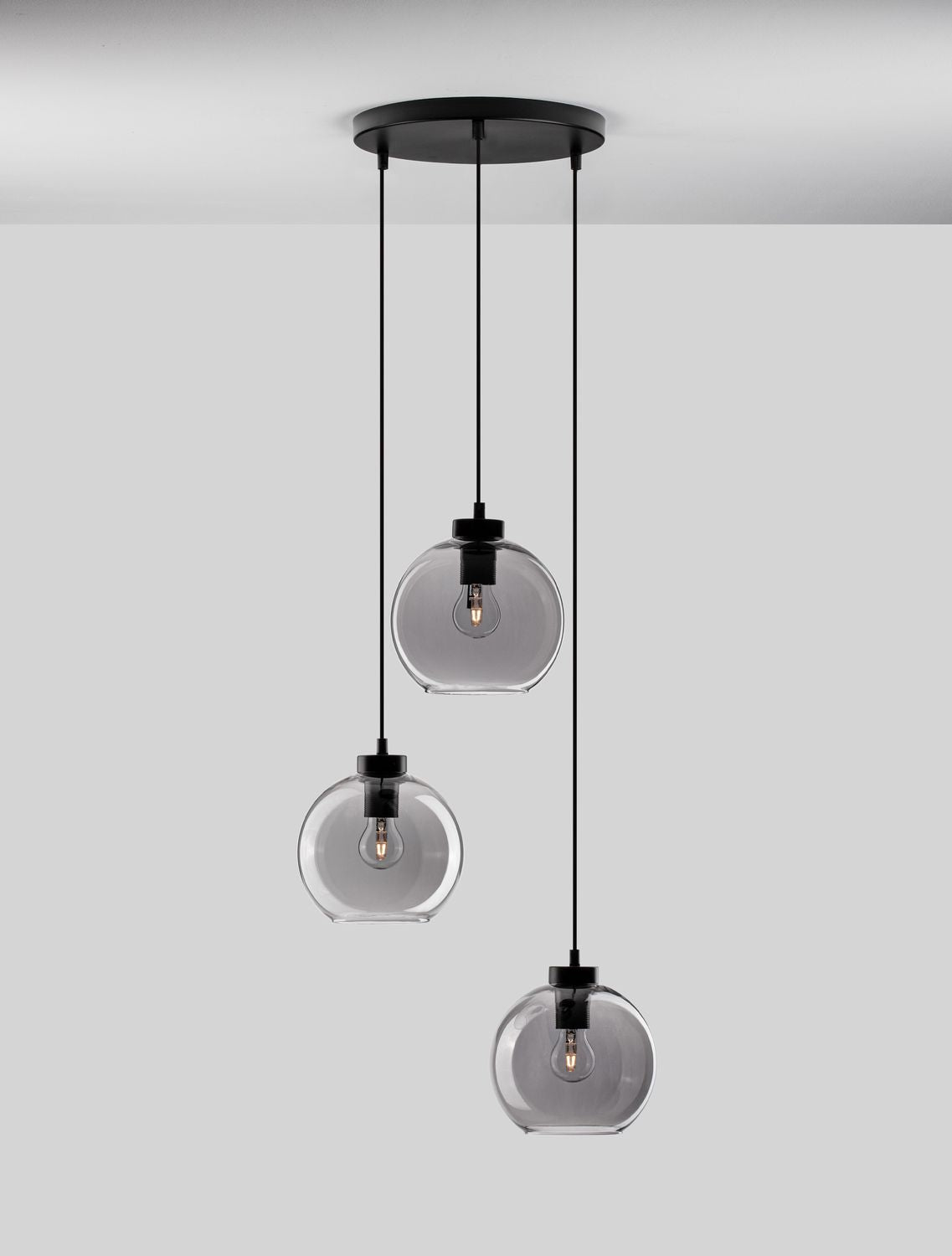Détail du luminaire : trois globes en verre fumé avec ampoules allumées et douilles noires.