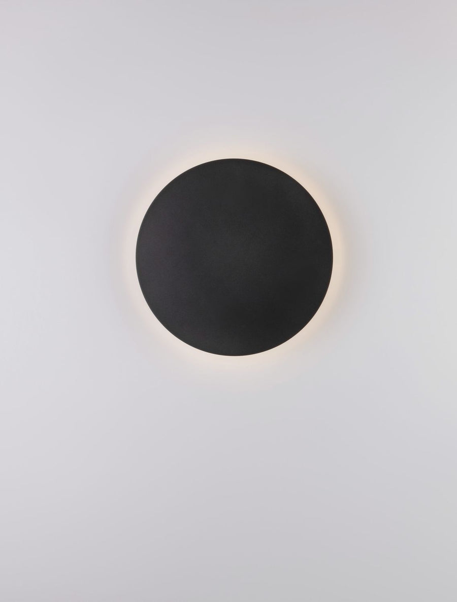 Disque noir en applique, éclairage indirect formant une couronne lumineuse chaude