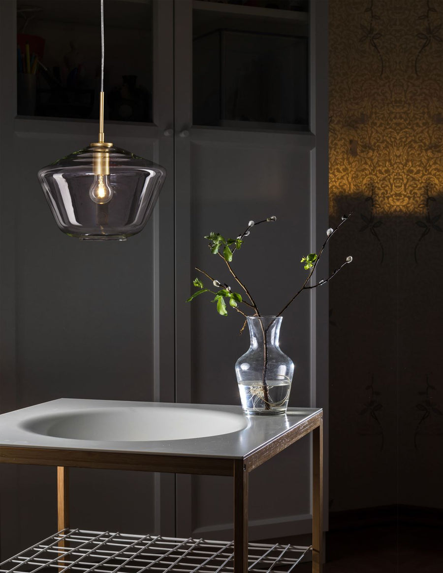 Suspension dorée en verre transparent éclairée, posée au-dessus d'une table avec vase