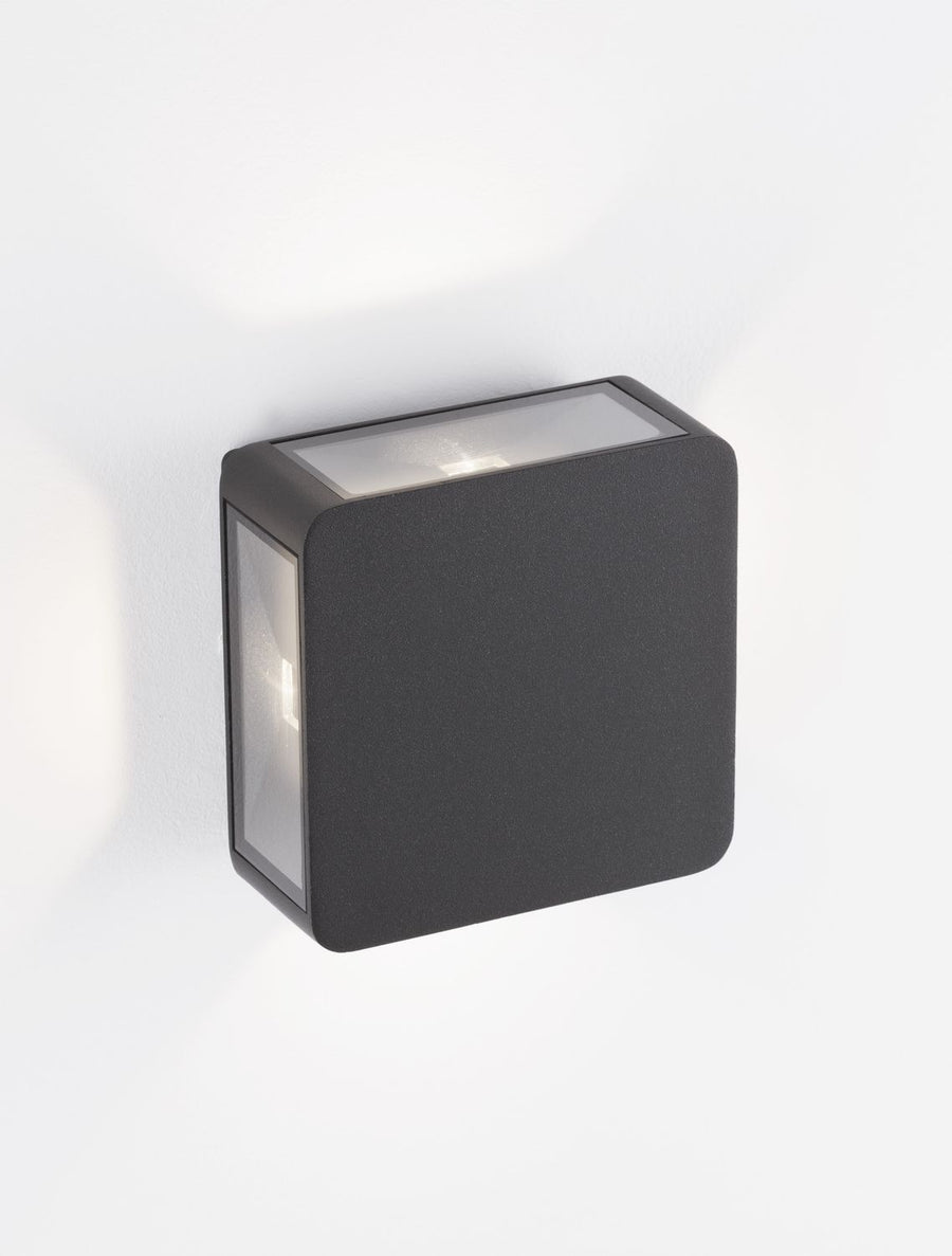 Vue trois quarts de l'applique murale anthracite carrée fixée sur un mur blanc