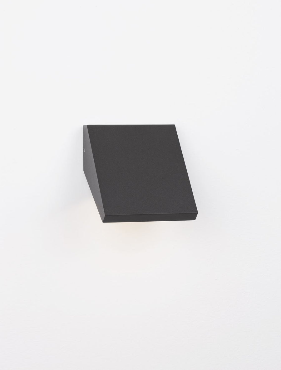 Vue rapprochée de l'applique allumée, lumière rasante sous le bloc anthracite.