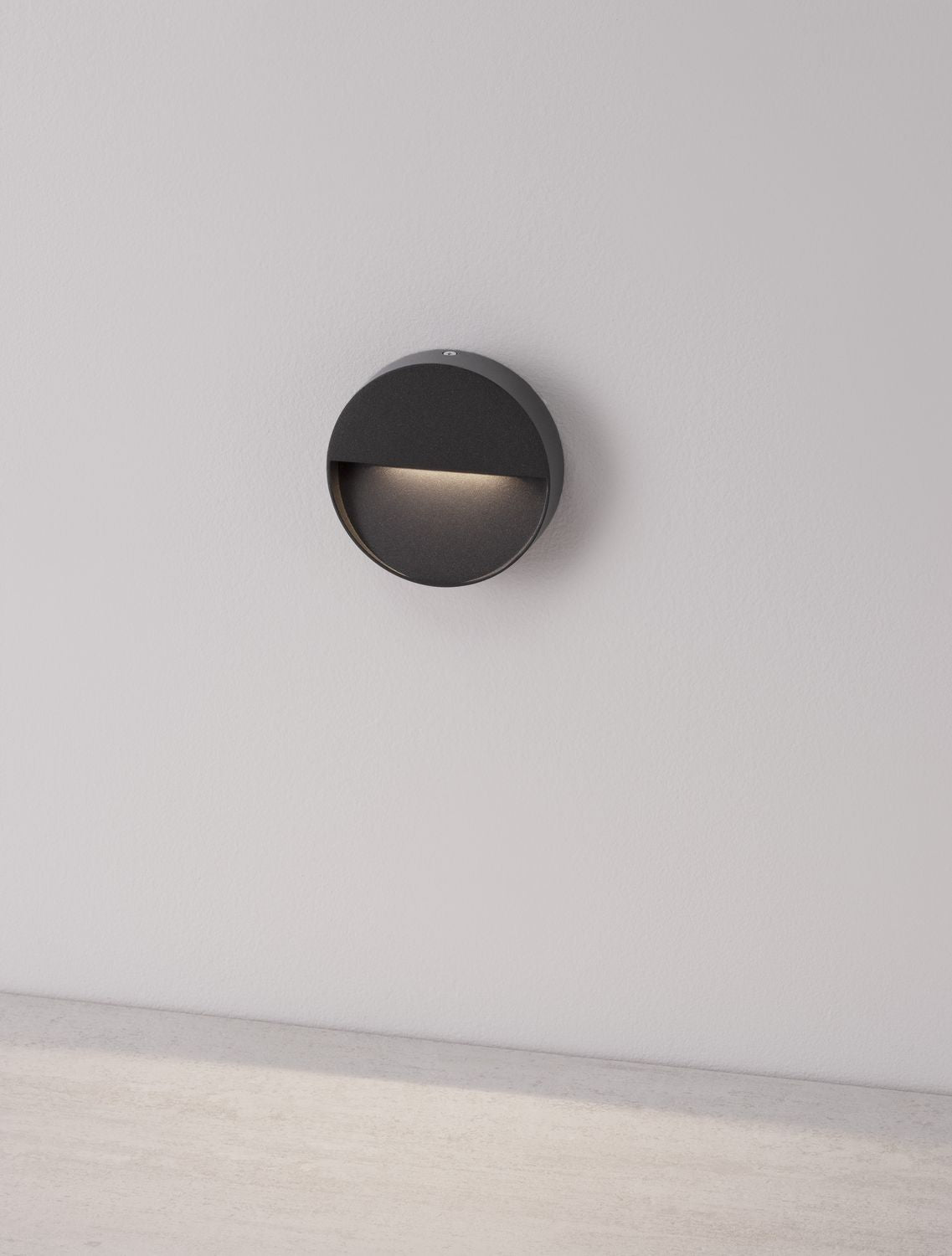 Applique murale ronde éclairée, diffusant une lumière rasante sur un mur blanc.