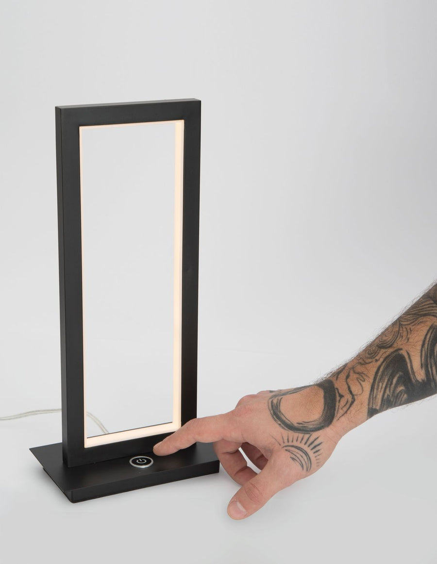 Main tatouée touchant le bouton tactile rond fixé sur la base du luminaire.