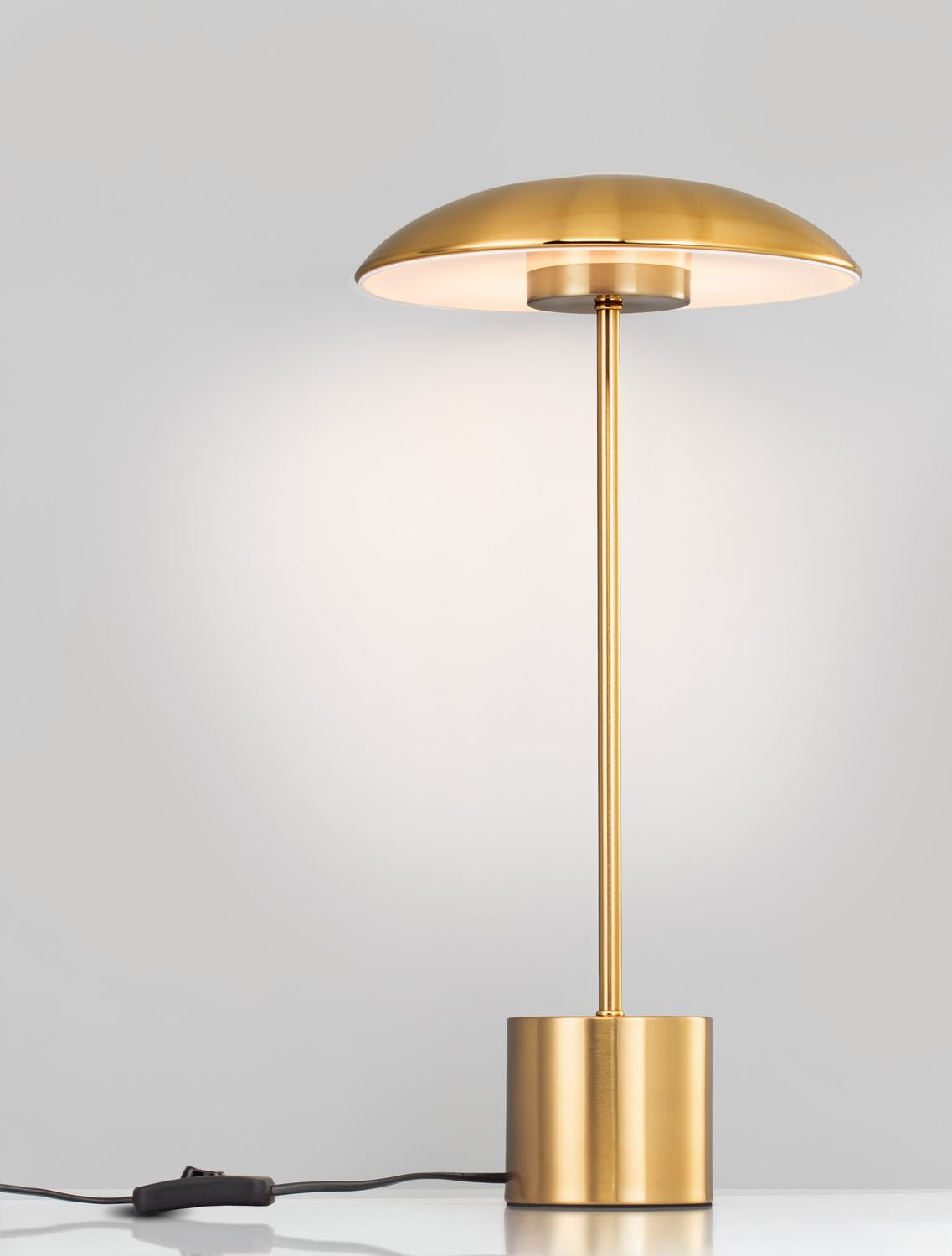Vue de trois quarts du luminaire doré avec câble et interrupteur sur table.