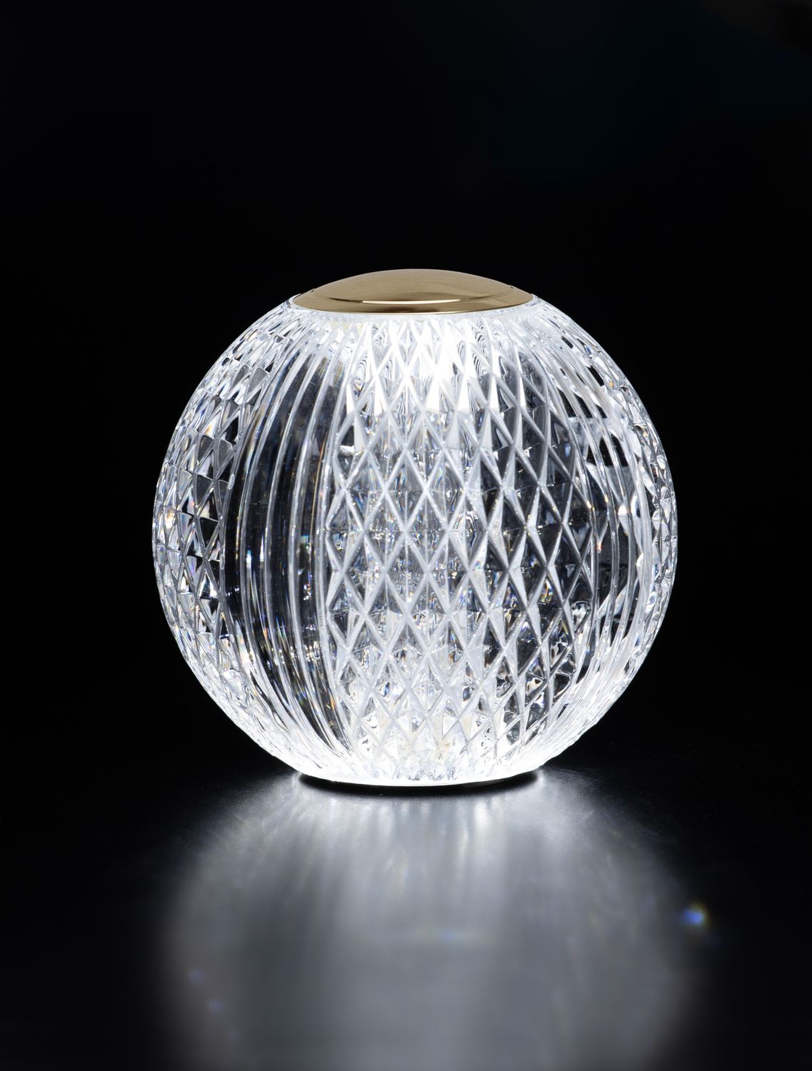 Photo sur fond noir, lampe allumée en contre-jour, reflets dorés et transparence du verre.