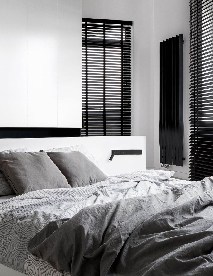Applique murale noire installée au-dessus d'un lit dans une chambre minimaliste.