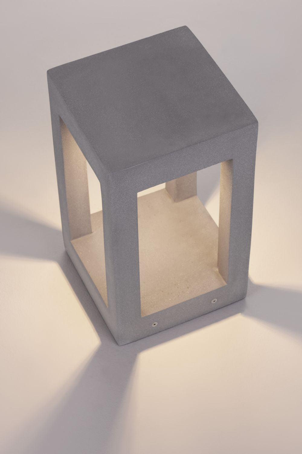 Vue trois quarts en ambiance beige, structure grise et volume intérieur ivoire du luminaire.