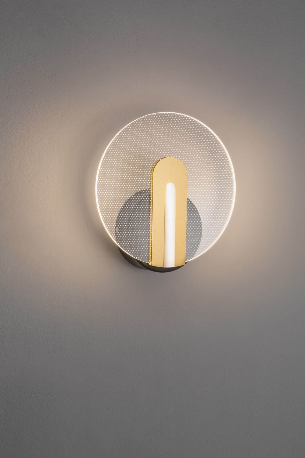 Applique murale allumée, halo lumineux sur mur gris, face avant du produit.