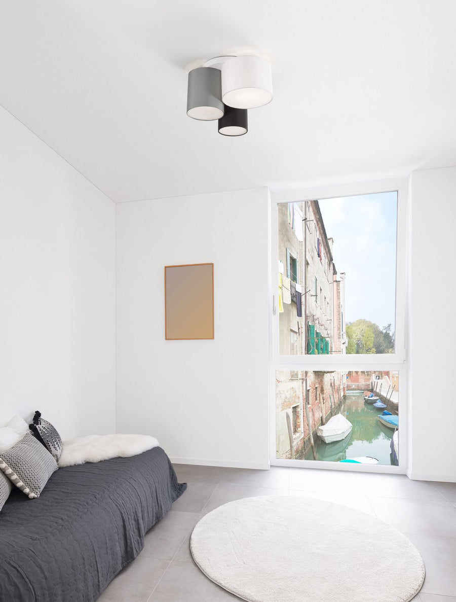 Plafonnier trois cylindres fixé au plafond d'une chambre blanche lumineuse