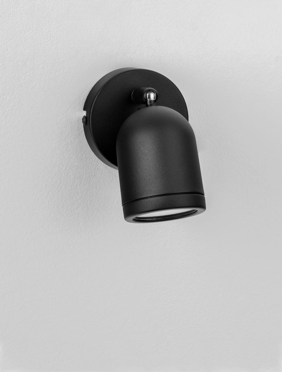 Détail du projecteur noir fixé sur une surface blanche, tête cylindrique inclinée vers le bas