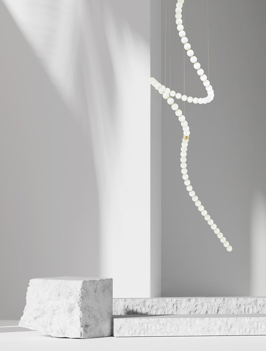 Suspension sculpturale en perles de verre blanc suspendue dans un décor minimal aux blocs de pierre