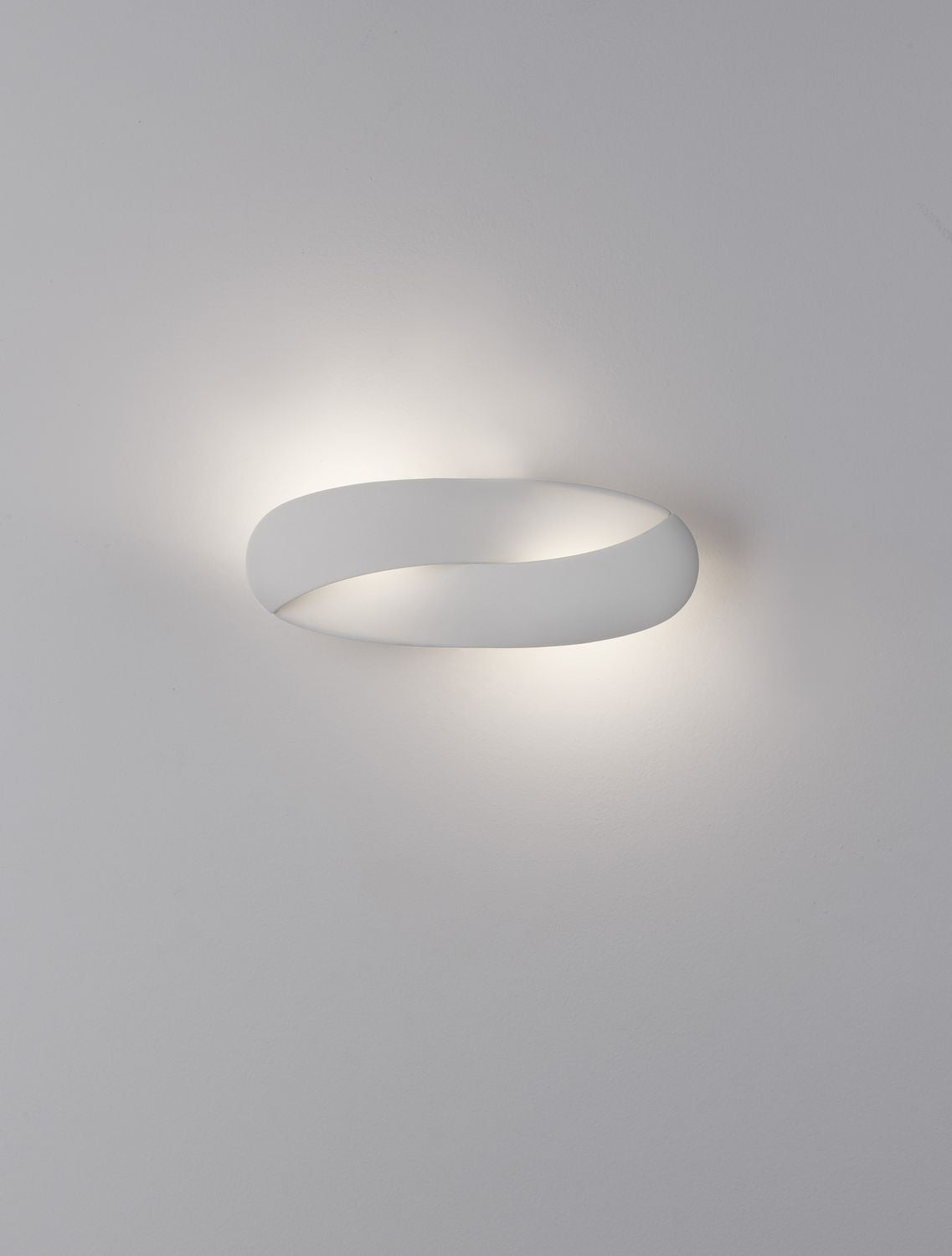Applique blanche allumée sur mur blanc, halo lumineux doux tout autour
