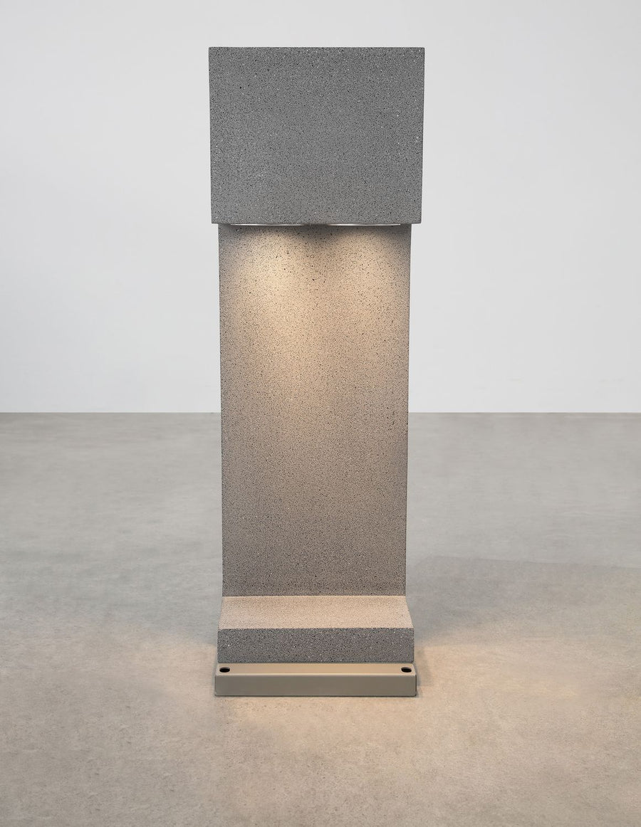Vue de face de la borne en béton gris, lumière allumée sur sol gris
