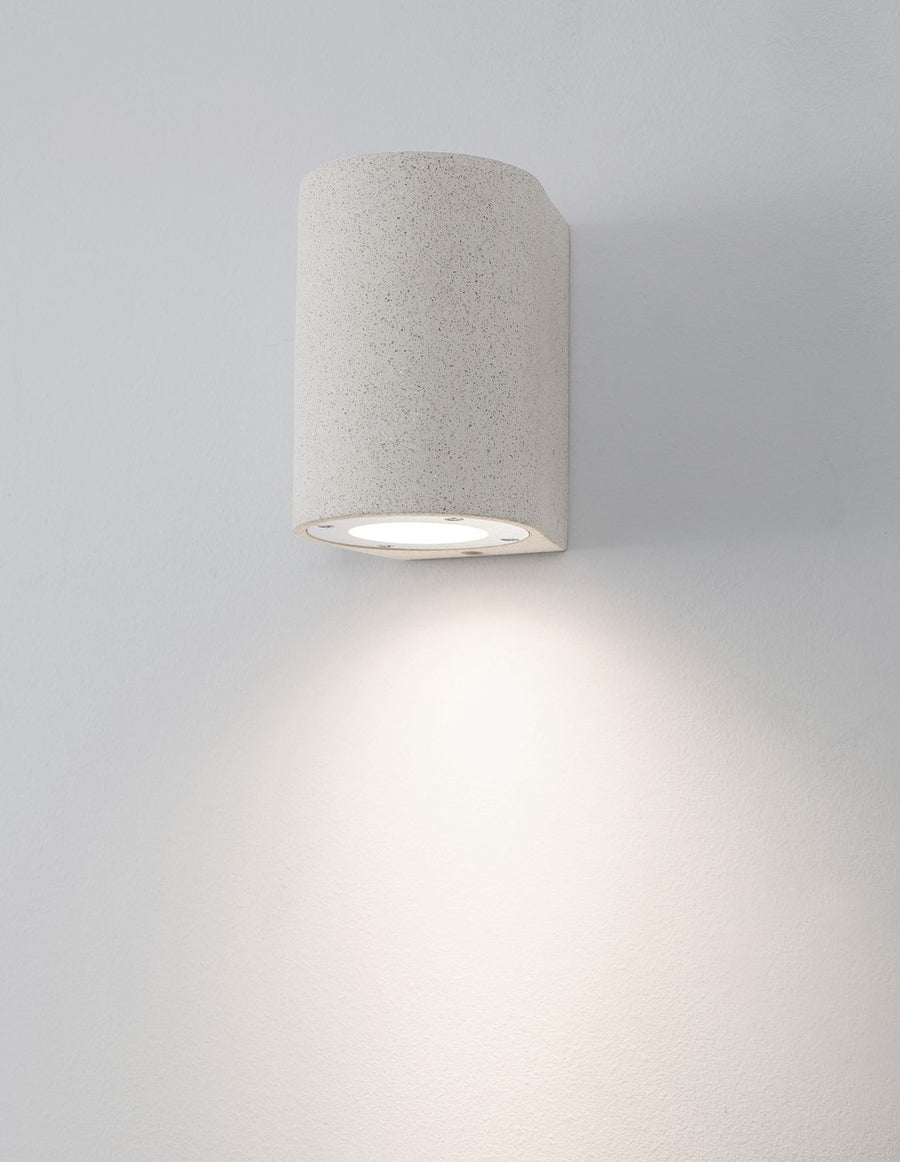 Applique murale blanche allumée sur mur clair, halo de lumière diffuse vers le bas.