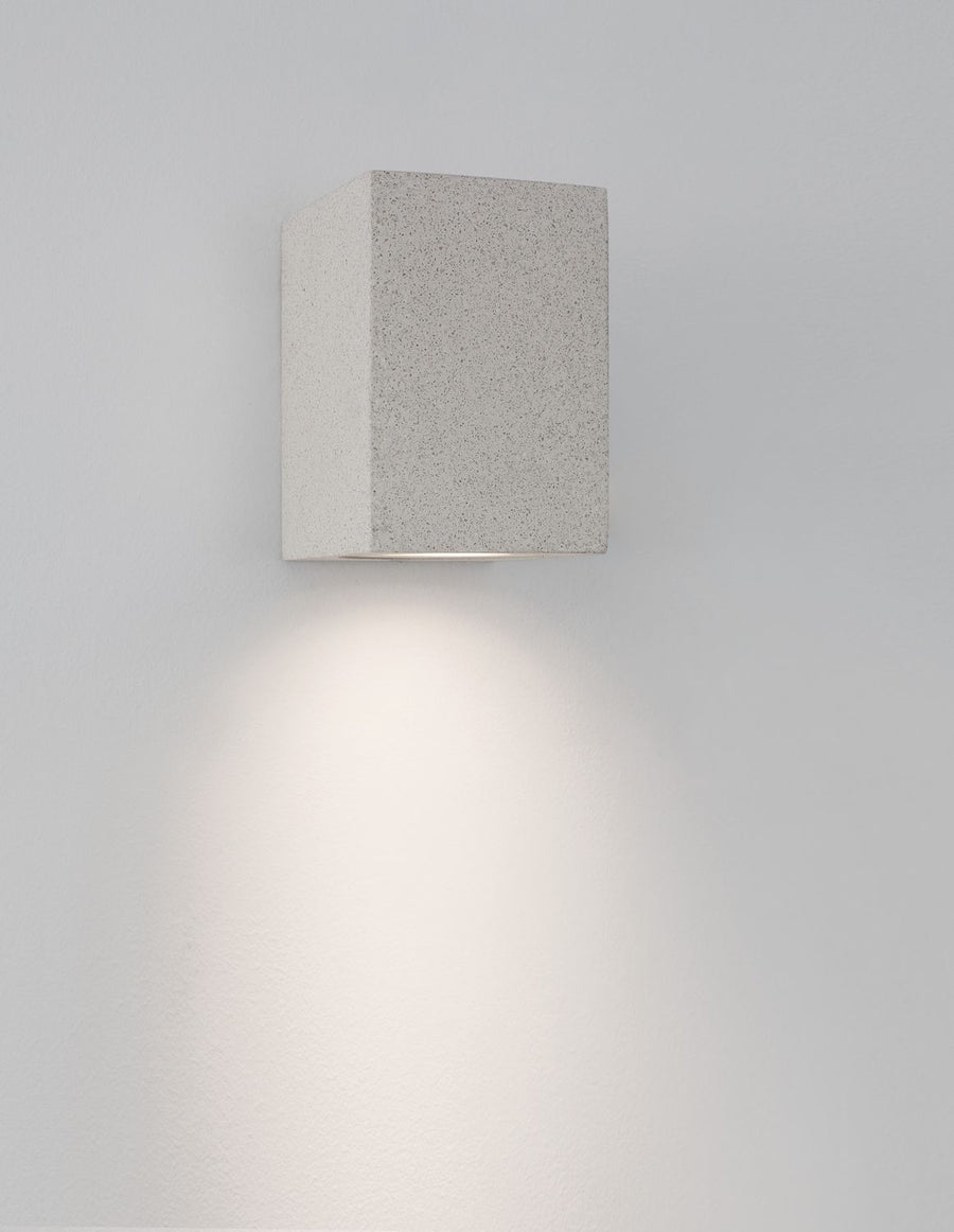 Luminaire mural allumé projetant une lumière chaude en cône sur le mur
