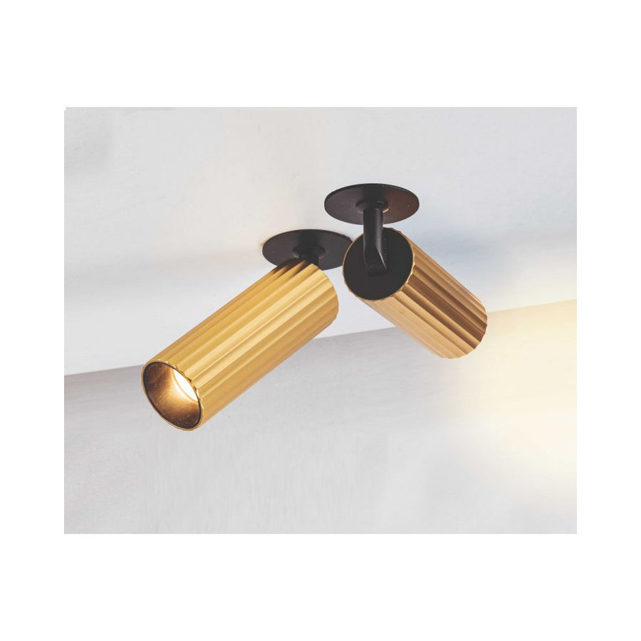 Deux plafonniers cylindriques dorés orientables fixés au plafond, éclairant un mur blanc.
