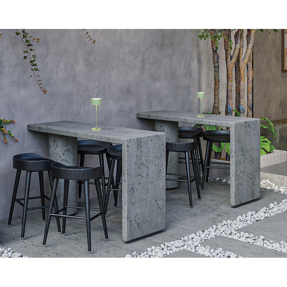 Mise en ambiance sur table haute en béton dans une cour extérieure avec tabourets noirs.