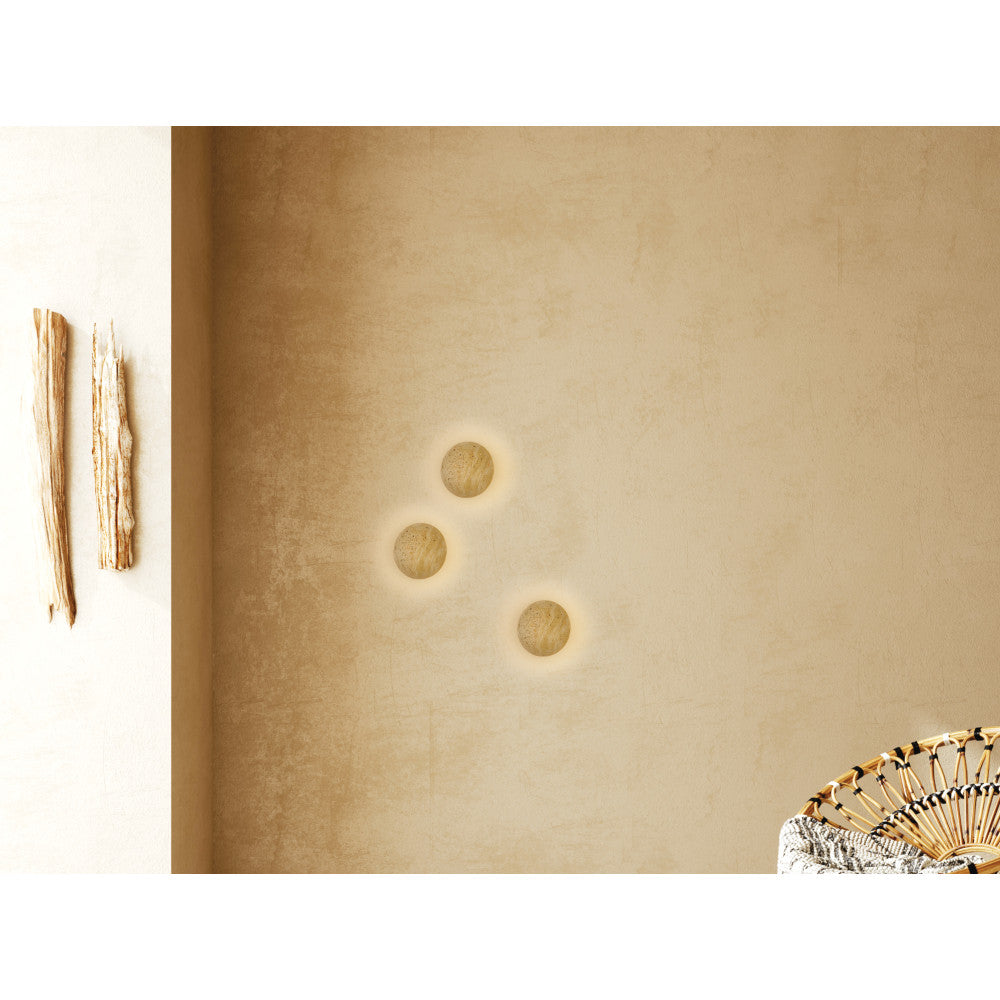 Trois appliques rondes allumées sur un mur beige, halo lumineux.