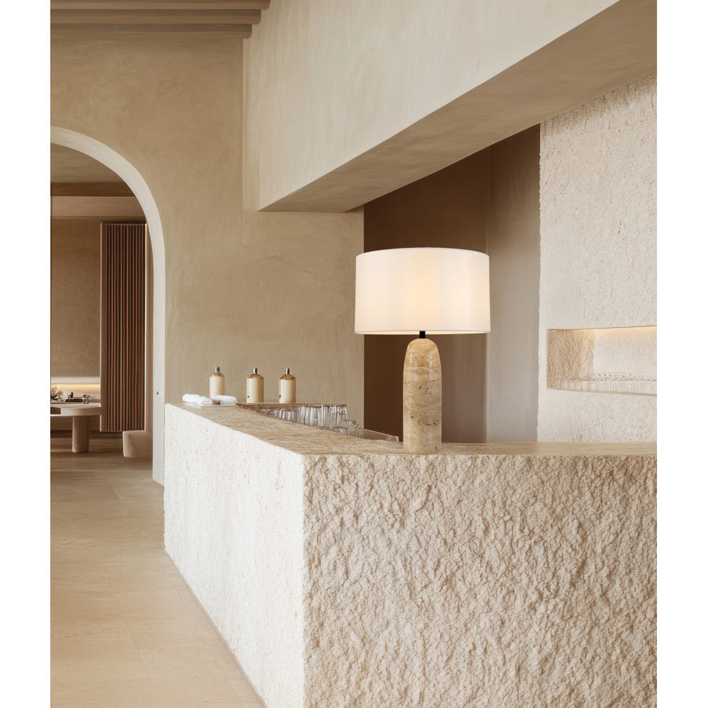 Mise en ambiance sur un comptoir en pierre, lampe allumée dans un intérieur beige minéral.