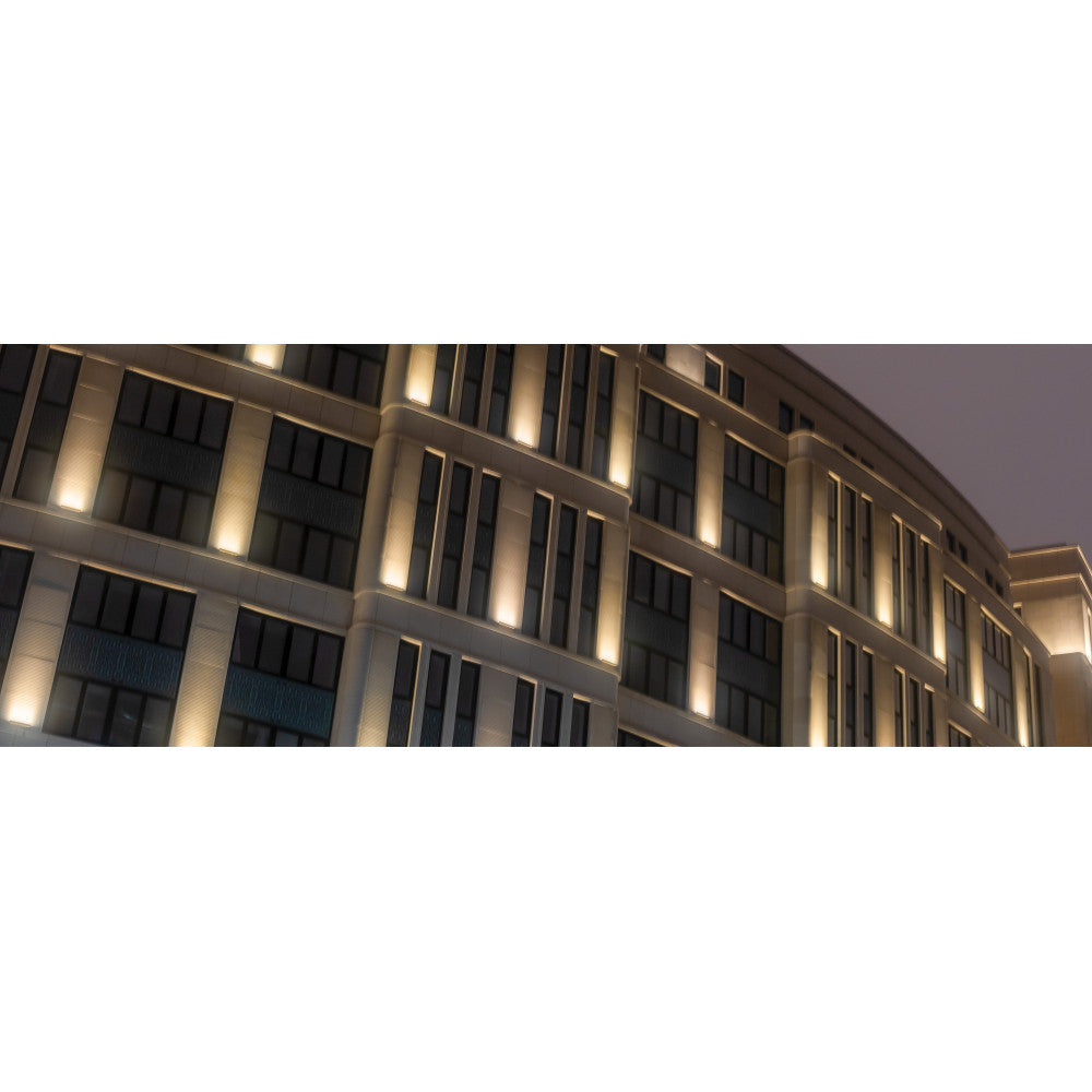 Façade d'immeuble éclairée de nuit par des luminaires linéaires verticaux.