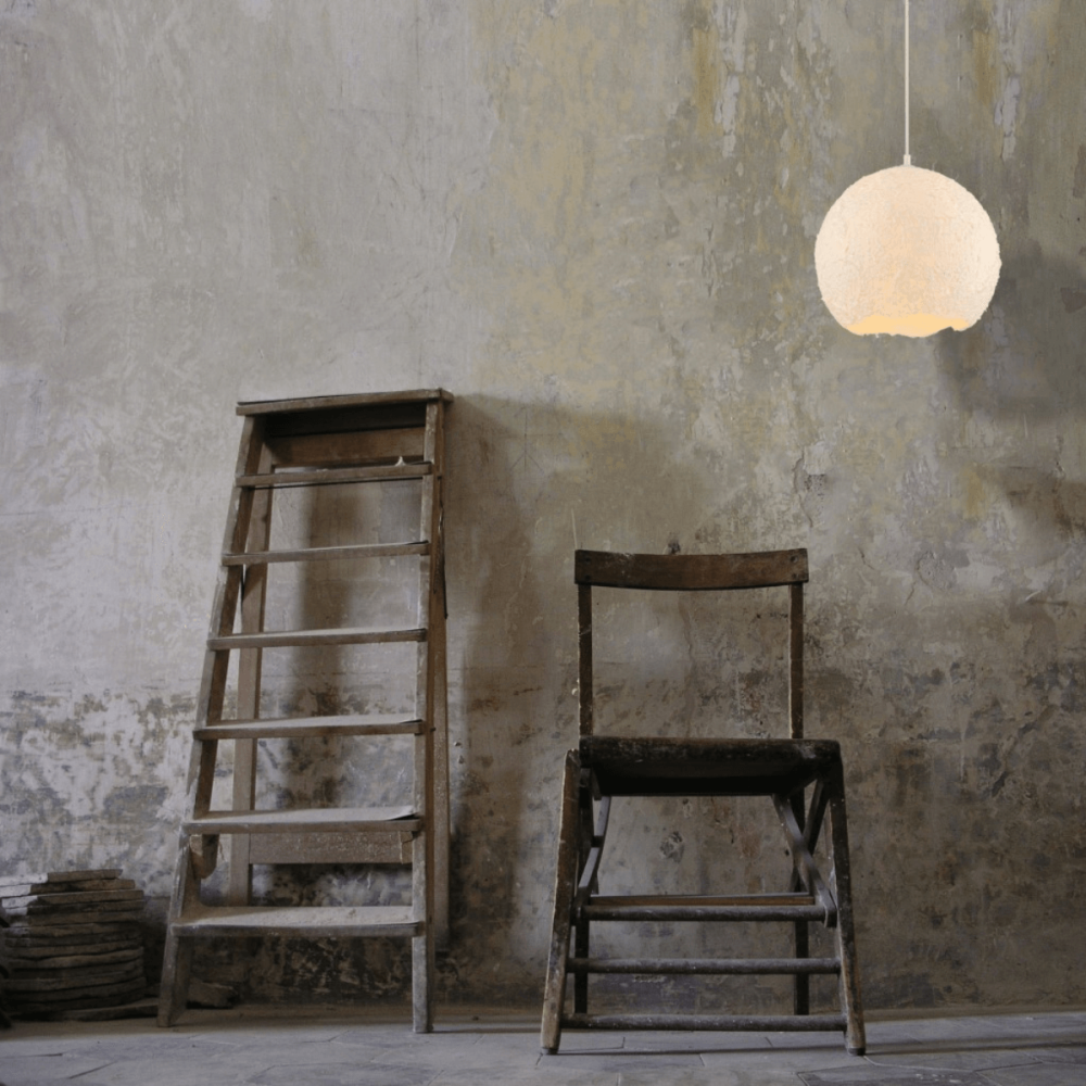 Luminaire suspendu éclairé dans un décor brut avec échelle et chaise en bois.