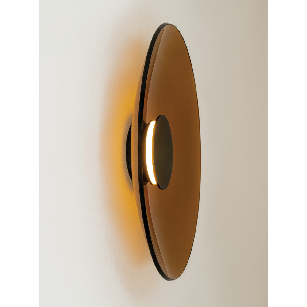 Profil de l'applique sur mur blanc, halo lumineux diffus autour du disque