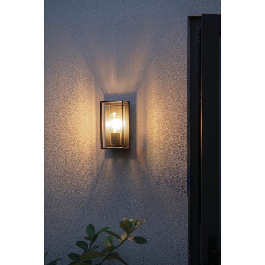 Applique allumée sur un mur extérieur texturé, lumière chaude et ombre portée.