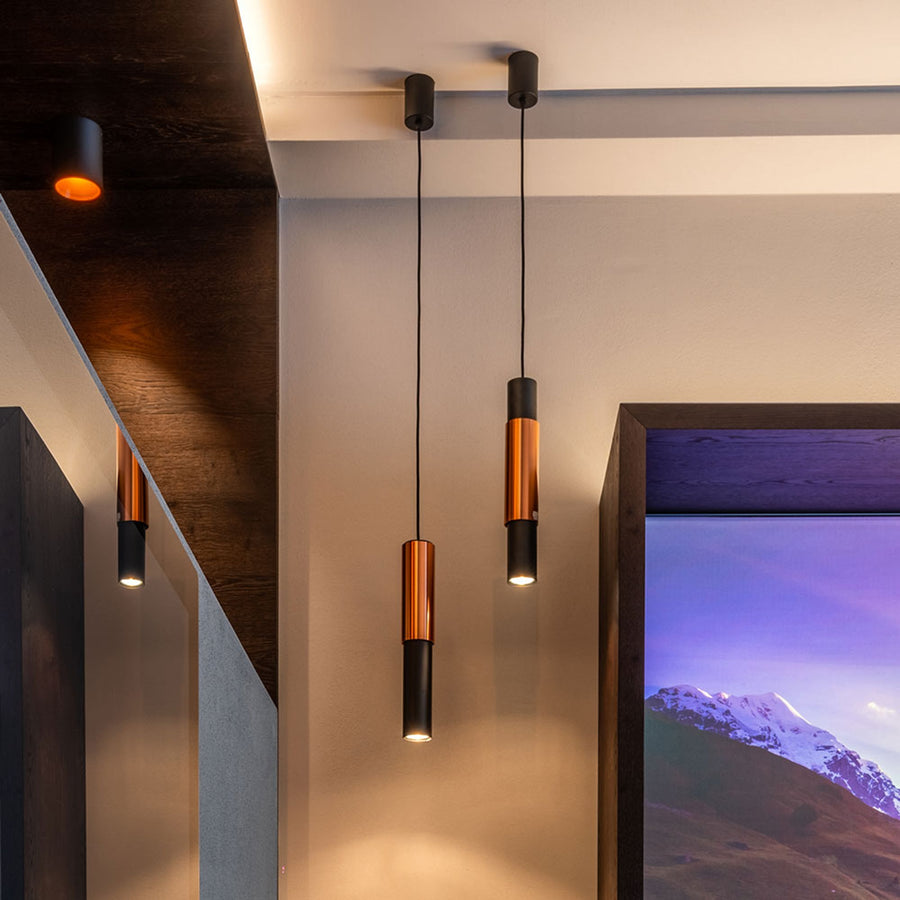 Suspensions cylindriques noires et cuivrées éclairant un intérieur moderne avec cadre montagneux.