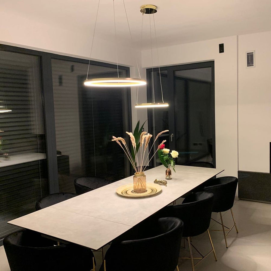 Deux suspensions dorées en anneau éclairent une salle à manger, au-dessus d'une grande table.