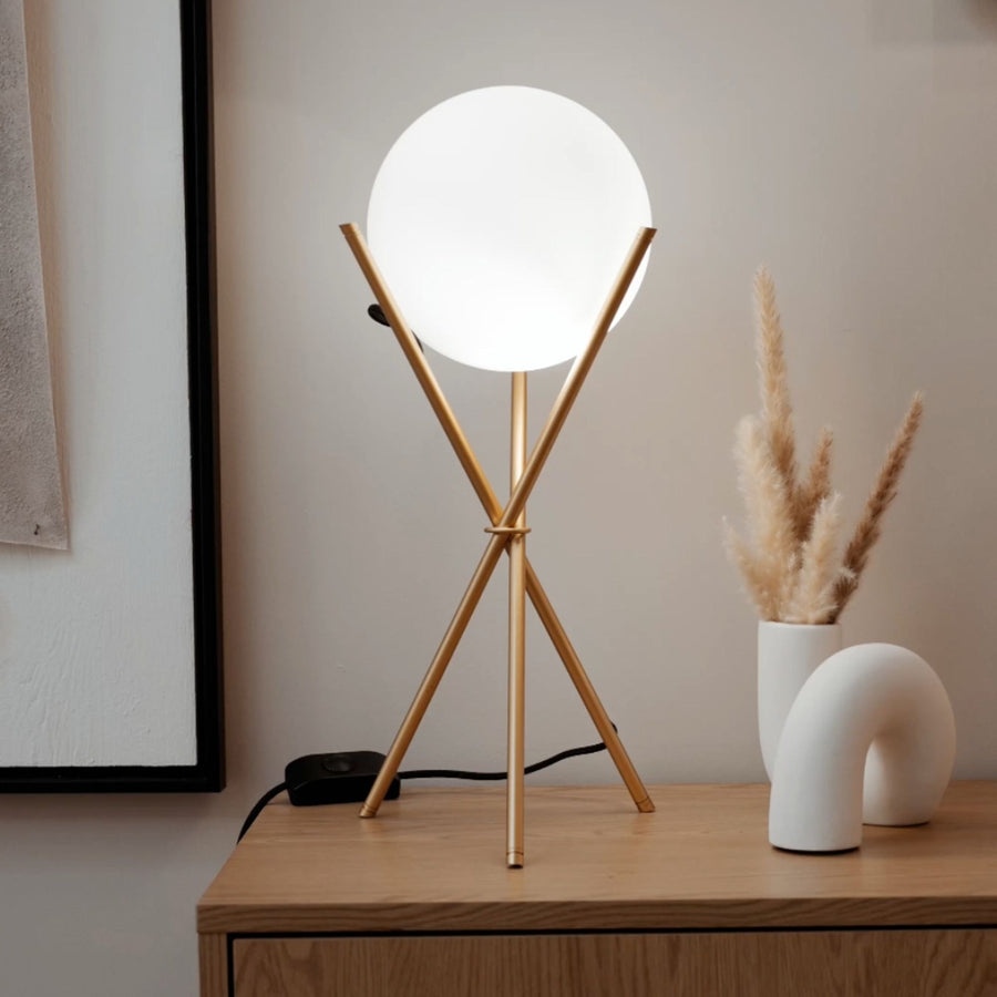 Lampe à poser trépied doré avec globe en verre blanc allumé sur un meuble en bois