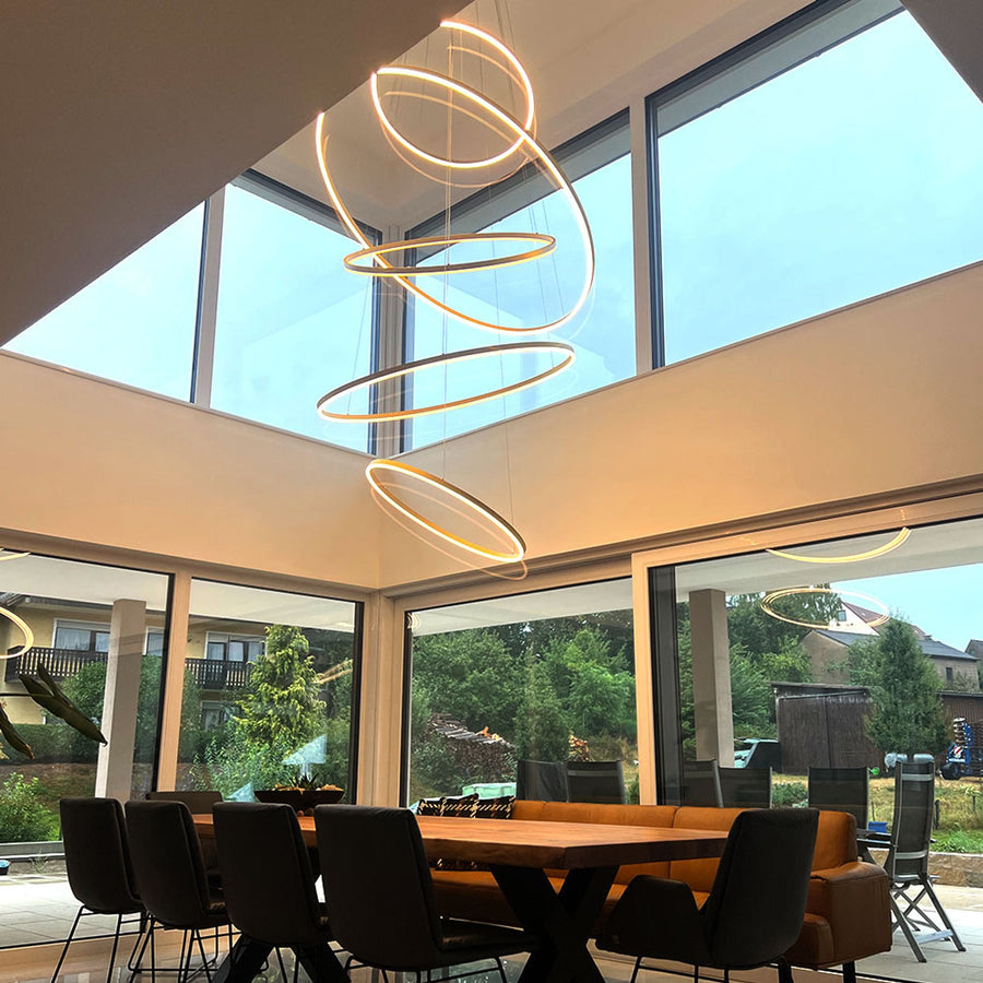 Salle à manger sous verrière avec anneaux dorés suspendus et vue sur le jardin