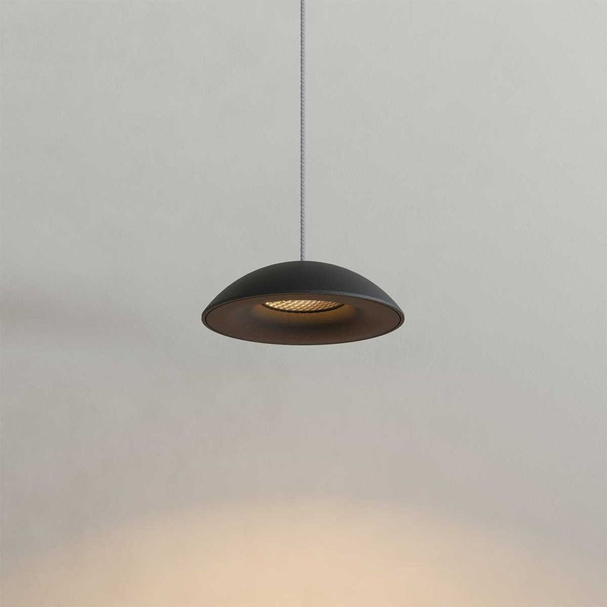 Gros plan sur un luminaire noir suspendu, montrant la coupole et le réflecteur interne éclairé.