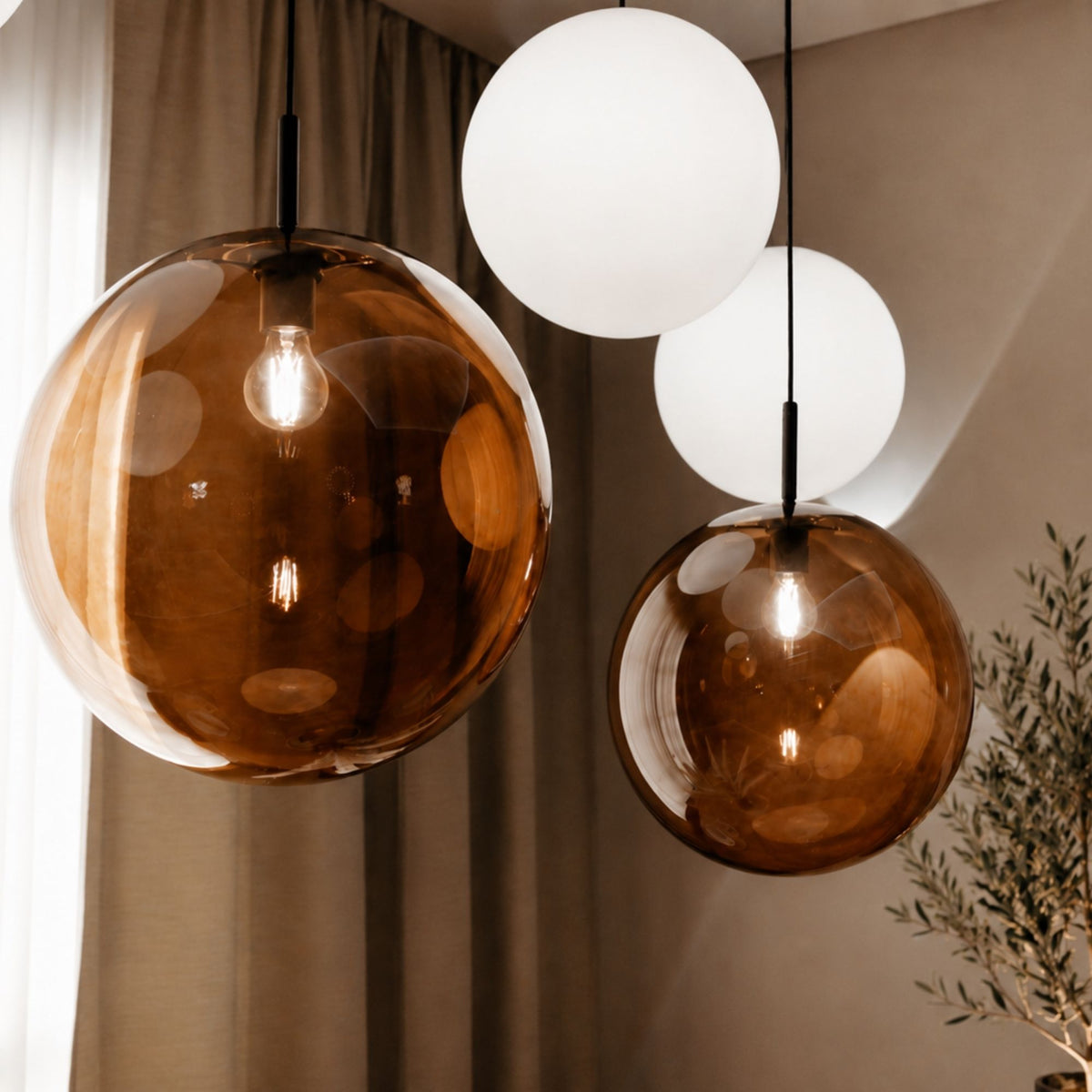 Gros plan sur des globes en verre ambré et blanc, ampoules visibles, devant des rideaux.