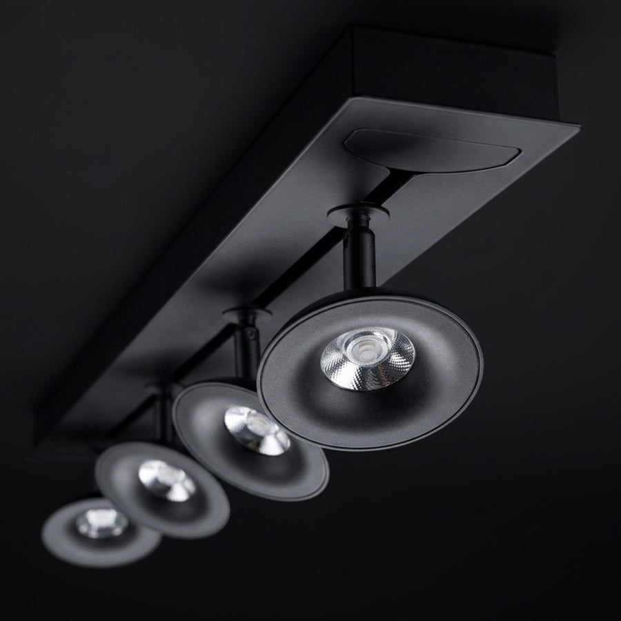 Rail noir avec quatre spots orientables alignés, vus de dessous sur fond sombre