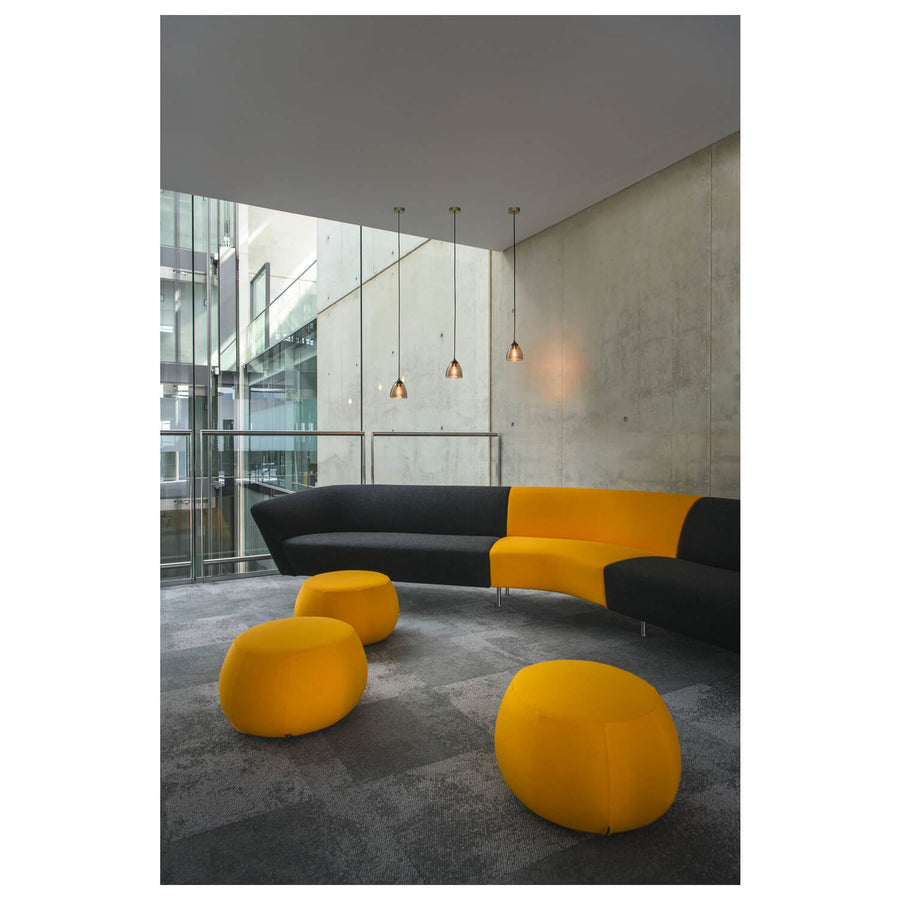 Trois suspensions éclairées dans un hall moderne, au-dessus d’une banquette jaune et noire.