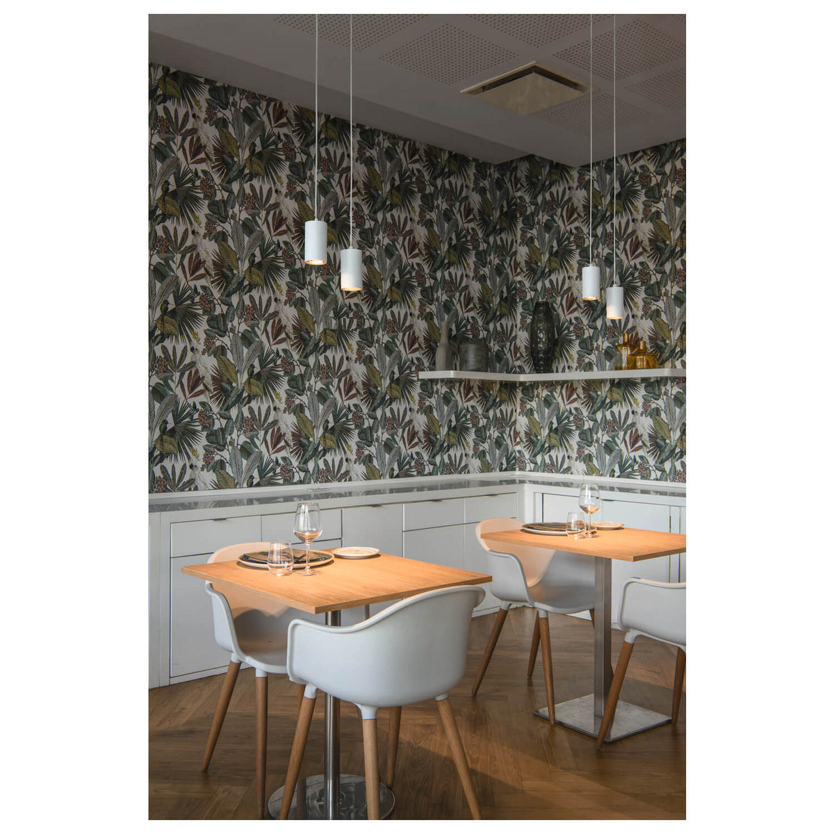 Mise en ambiance dans un restaurant avec papier peint tropical et suspensions blanches alignées